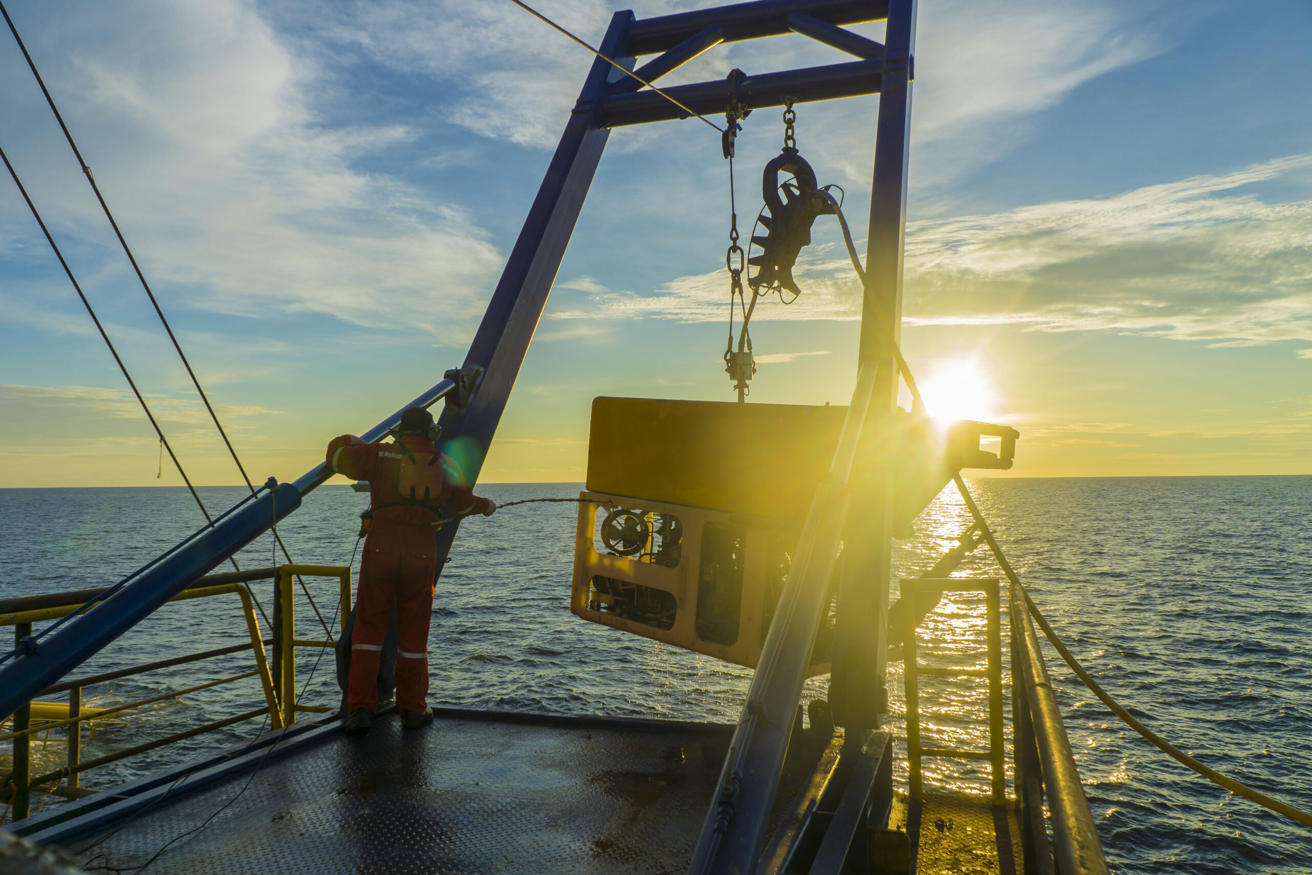 Worker recovering remote operated vehicle from sea with crane