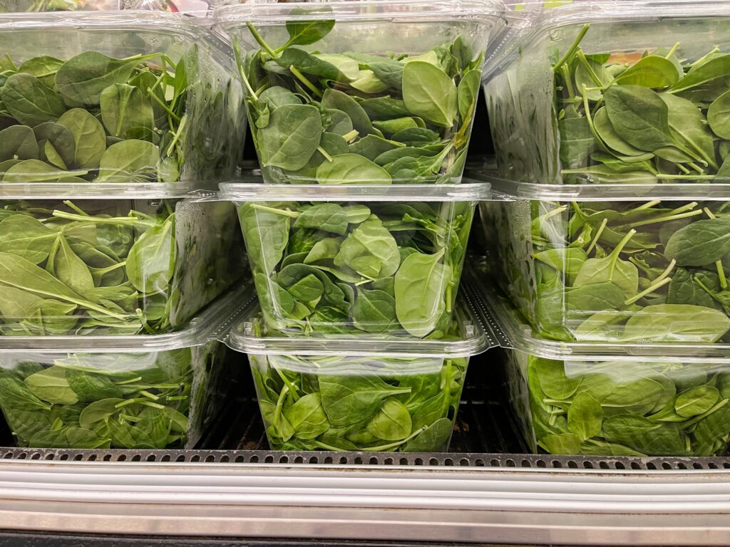 Close up of spinach packaged in clear plastic thermoformed containers in a fridge