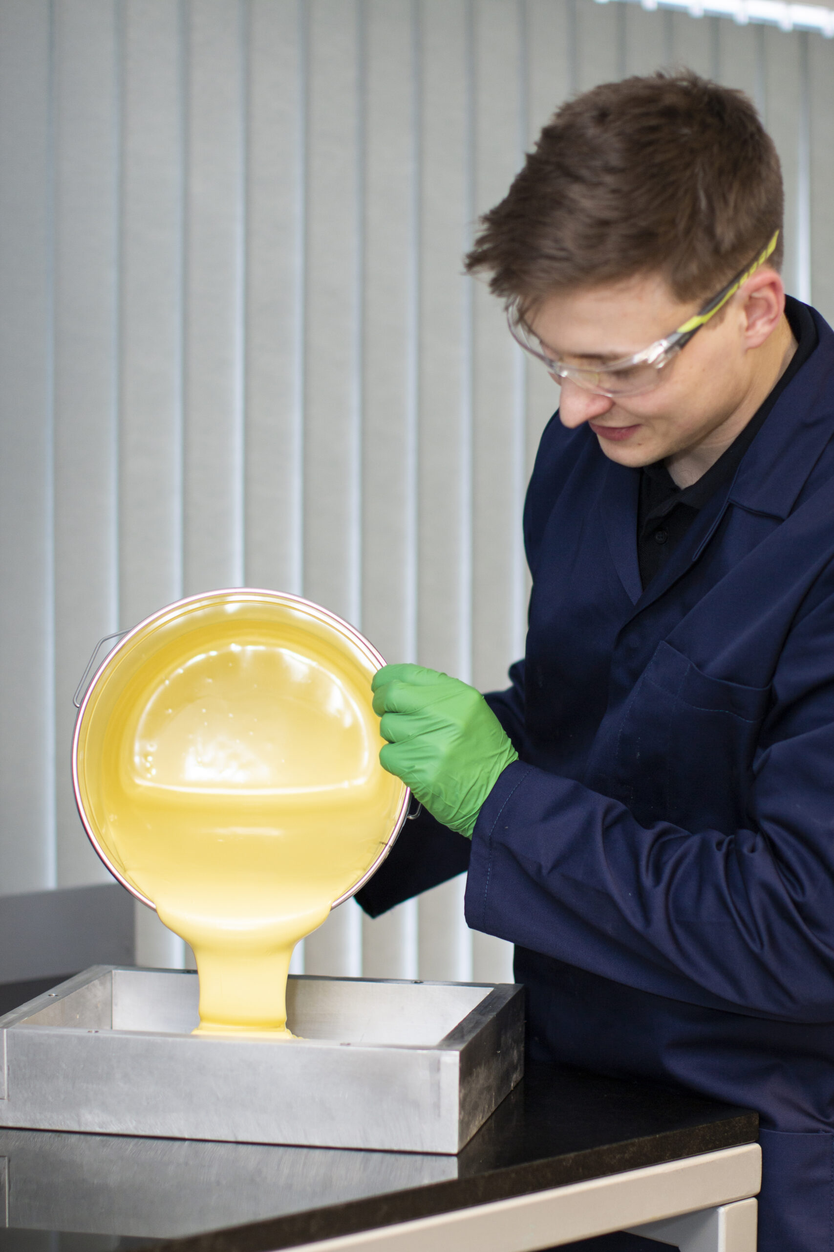 Man wearing laboratory safety equipment pouring tooling material into a mold