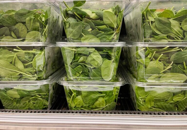 Close up of spinach packaged in clear plastic thermoformed containers in a fridge