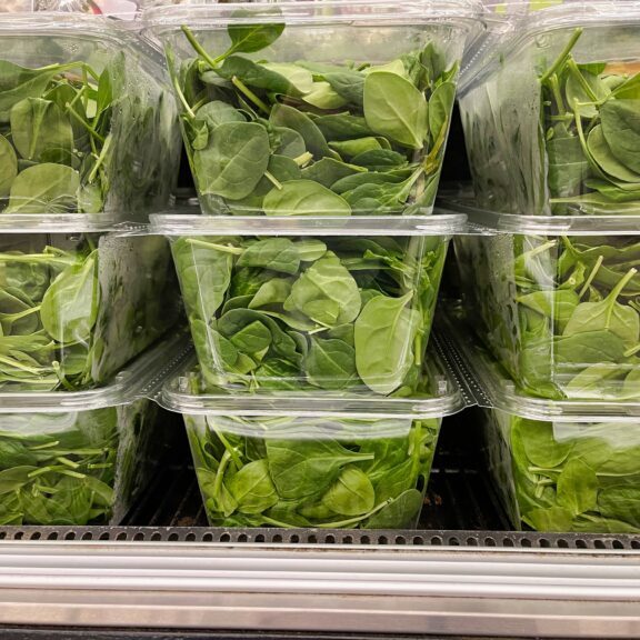 Close up of spinach packaged in clear plastic thermoformed containers in a fridge