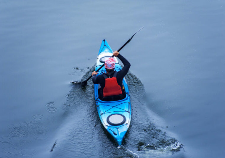 Man paddling in a blue kayak on a river
