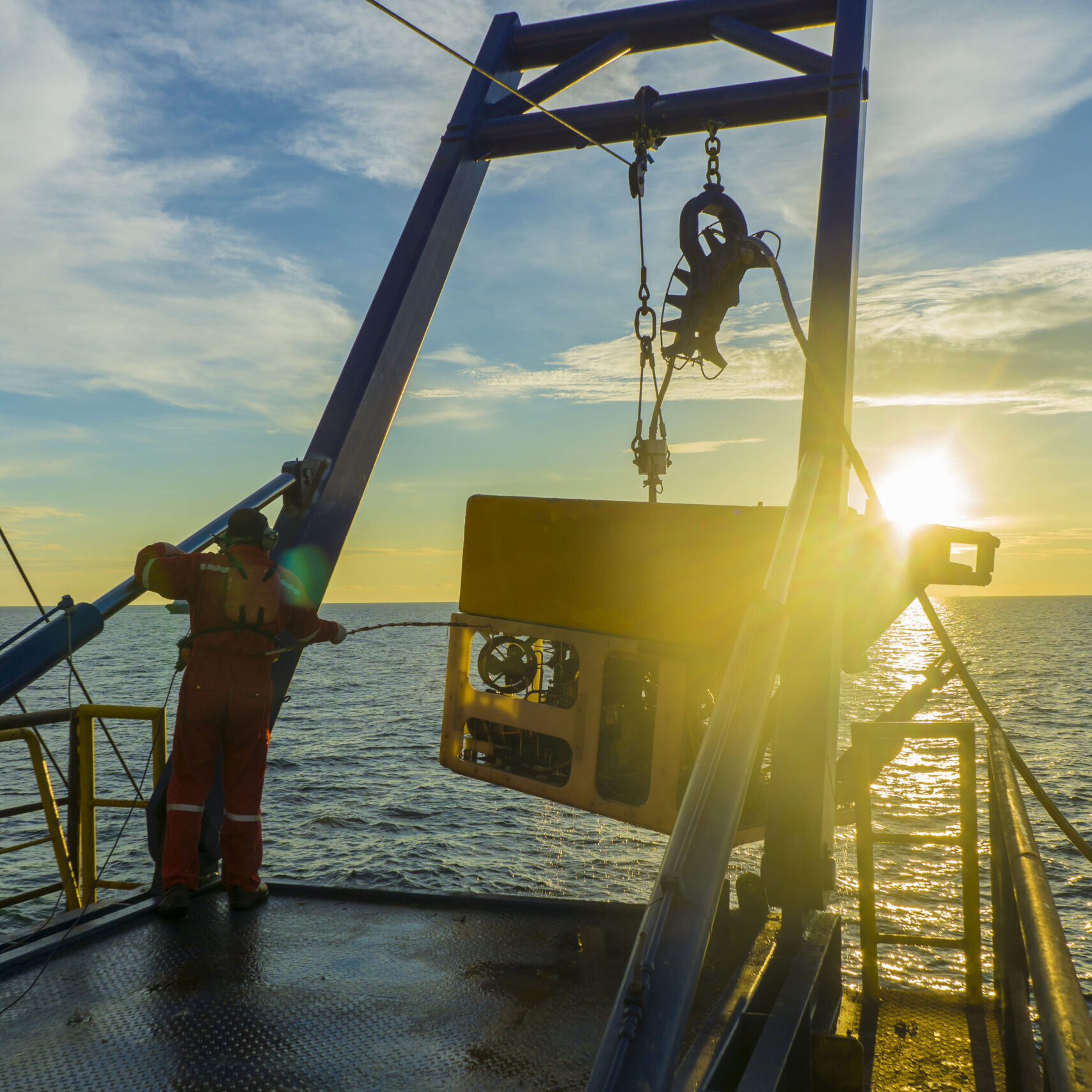 Worker recovering remote operated vehicle from sea with crane