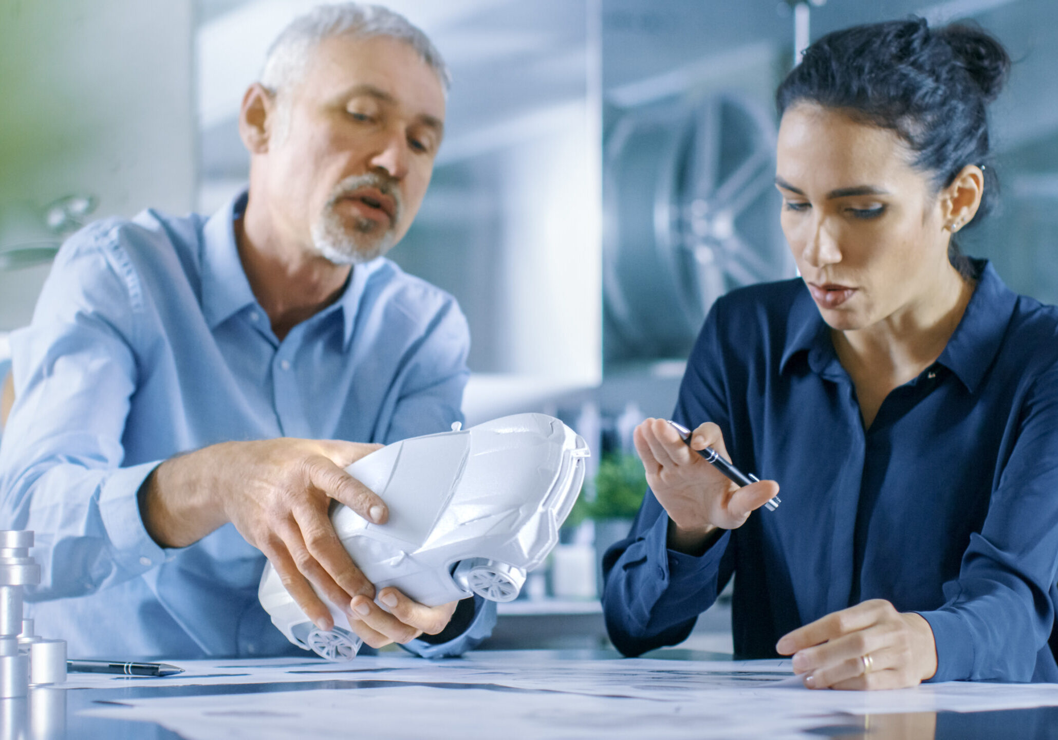 Automotive designer and engineer sat at a table looking over a concept car model