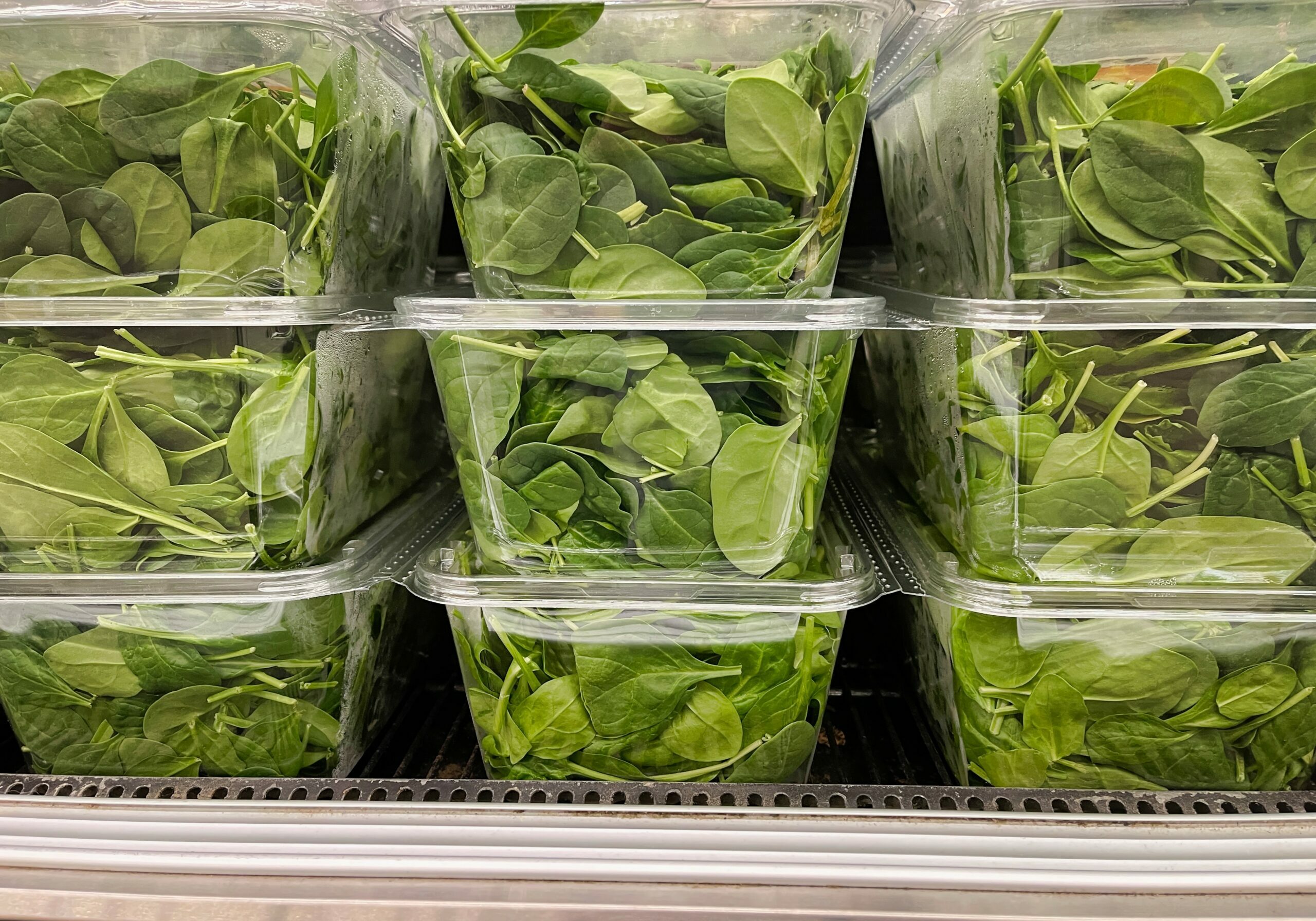 Close up of spinach packaged in clear plastic thermoformed containers in a fridge